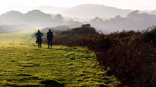 Two visitors walk along the South West Coast Path to Old Harry with misty views behind them, at Studland Bay, Dorset